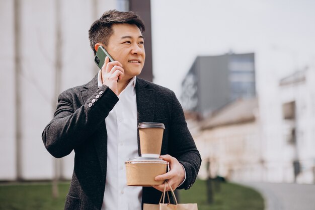 Hombre de negocios asiático con comida para llevar, hablando por teléfono