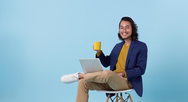 hombre de negocios asiático feliz sonriendo usando computadora portátil sentado en una silla blanca y tomando café