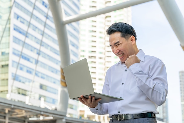 Hombre de negocios asiático con ordenador portátil en el distrito de negocios urbano - concepto de gente de negocios de estilo de vida