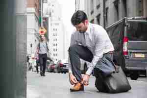 Foto gratuita hombre de negocios atar cordones cerca de la carretera