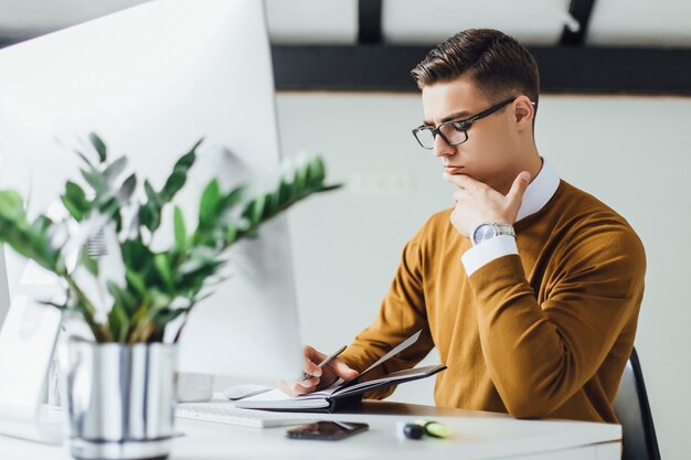 Hombre de negocios atractivo y creativo con ordenador portátil escribiendo notas en la oficina