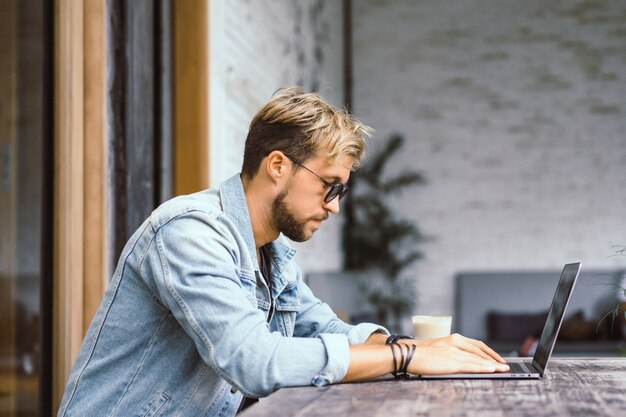 El hombre de negocios atractivo joven en un café trabaja para una computadora portátil, bebe café.