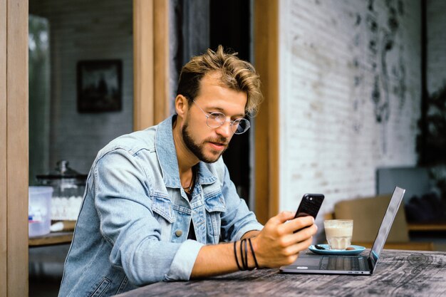 El hombre de negocios atractivo joven en un café trabaja para una computadora portátil, bebe café.