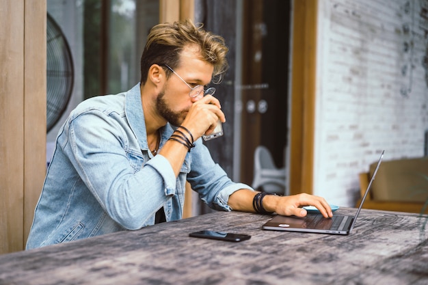 El hombre de negocios atractivo joven en un café trabaja para una computadora portátil, bebe café.