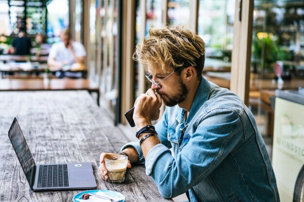 El hombre de negocios atractivo joven en un café trabaja para una computadora portátil, bebe café.