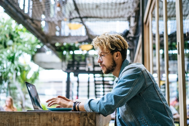 El hombre de negocios atractivo joven en un café trabaja para una computadora portátil, bebe café.