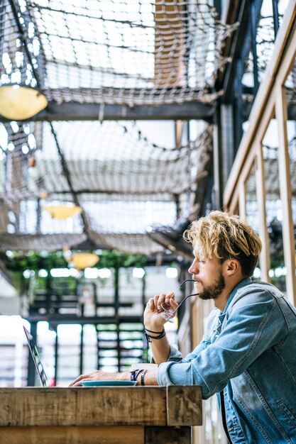 El hombre de negocios atractivo joven en un café trabaja para una computadora portátil, bebe café.