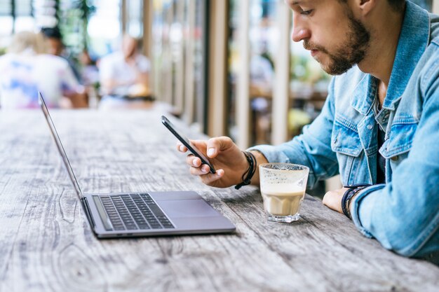 El hombre de negocios atractivo joven en un café trabaja para una computadora portátil, bebe café.