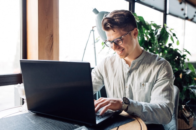 Hombre de negocios atractivo en lentes que trabaja en la computadora portátil, escribiendo, pasando tiempo en el café.