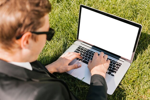 Hombre de negocios de Backview que usa el ordenador portátil en hierba verde