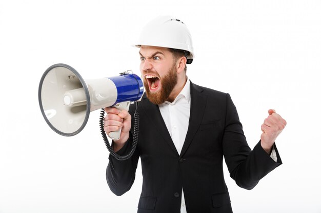 Hombre de negocios barbudo enojado en casco protector gritando en megáfono