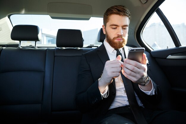 Hombre de negocios barbudo guapo en traje mediante teléfono móvil