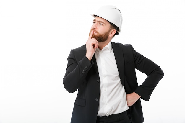 Foto gratuita hombre de negocios barbudo pensativo en casco protector mirando a otro lado