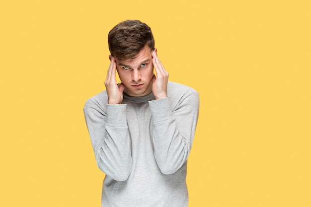 Hombre de negocios cansado o el joven serio sobre pared amarilla con emociones de dolor de cabeza