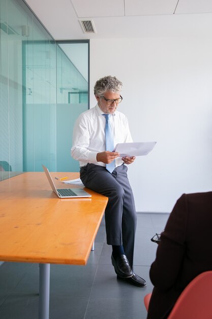 Hombre de negocios caucásico enfocado sentado en la mesa y leyendo el documento