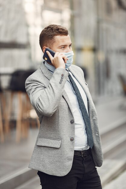 Hombre de negocios en una ciudad. Persona con máscara. Chico con teléfono.