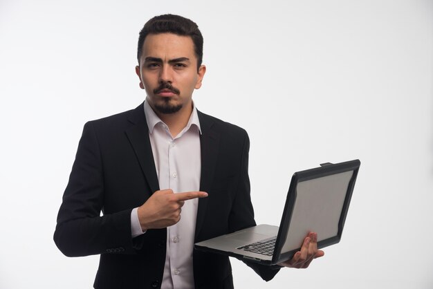 Un hombre de negocios en código de vestimenta sosteniendo una computadora portátil y apuntando a ella.