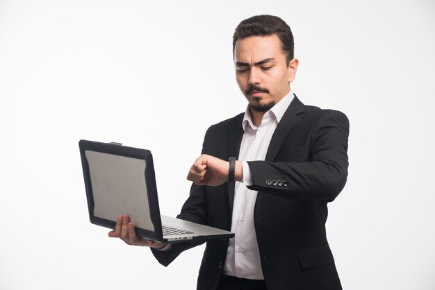 Un hombre de negocios en código de vestimenta sosteniendo una computadora portátil y controlando su tiempo.