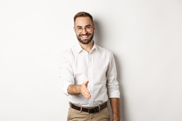 Hombre de negocios confiado que extiende la mano para el apretón de manos, saludando al socio comercial y sonriendo, de pie