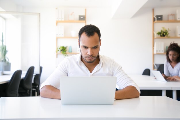 Hombre de negocios confiado serio que usa la computadora portátil en oficina