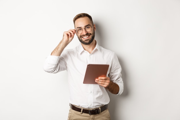 Hombre de negocios confiado trabajando en tableta digital, sonriendo feliz, de pie