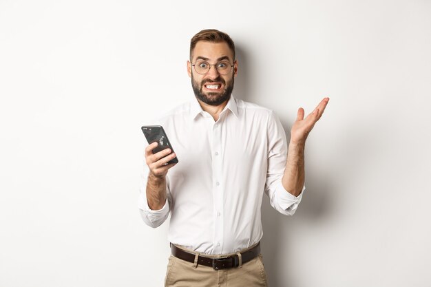 Hombre de negocios confundido leyendo un mensaje extraño en el teléfono móvil, mirando molesto, de pie.