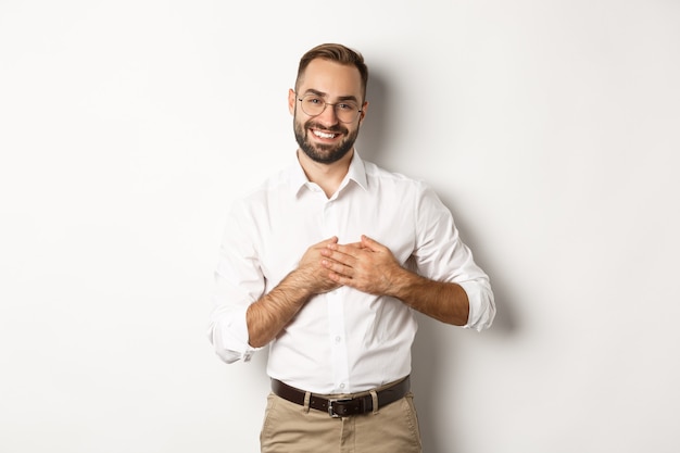 Hombre de negocios conmovido y agradecido cogidos de la mano en el corazón, sonriendo agradecido, de pie