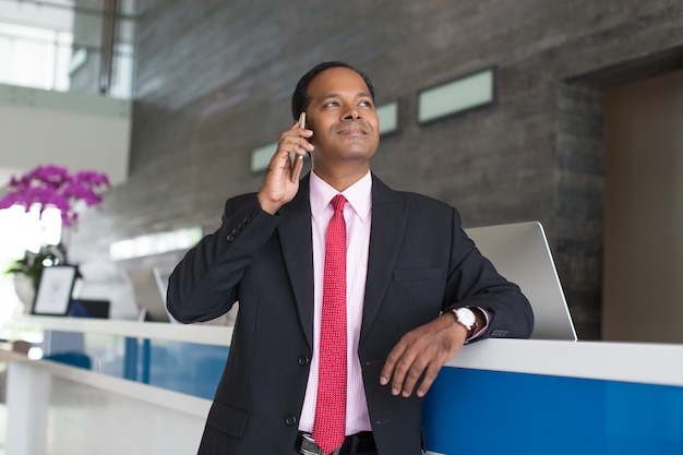 Hombre de negocios de contenido que llama en el teléfono en la recepción