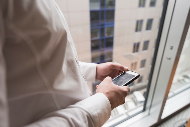 Hombre de negocios de la cosecha usando smartphone en la ventana