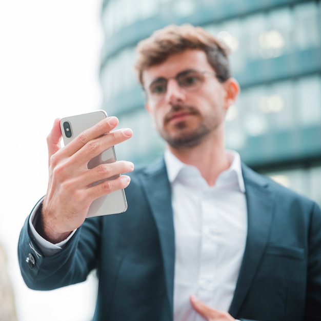 Hombre de negocios Defocused que mira el teléfono móvil que se coloca delante del edificio corporativo