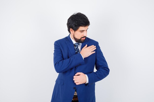 Hombre de negocios descansando la mano sobre el pecho en traje formal y mirando serio, vista frontal.