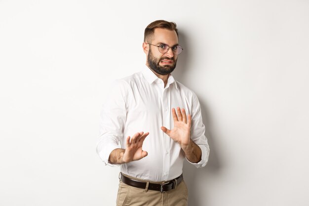 Hombre de negocios disgustado rechazando algo malo, encogiéndose de aversión, mostrando la señal de stop, de pie