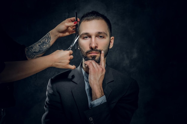 Un hombre de negocios elegante y confiado recibe un cuidado de la barba de una mujer con una bonita manicura.