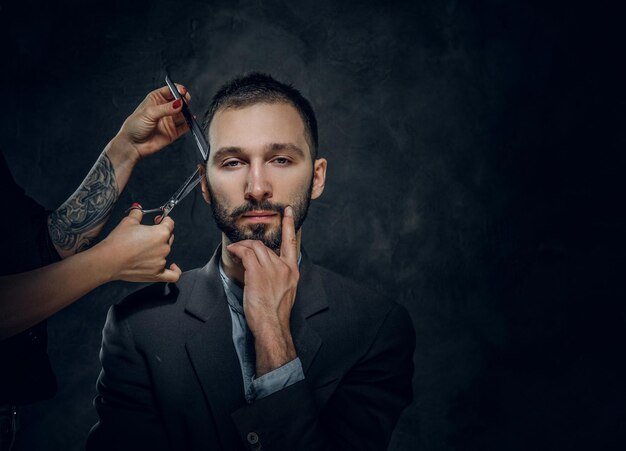 Un hombre de negocios elegante y confiado recibe un cuidado de la barba de una mujer con una bonita manicura.