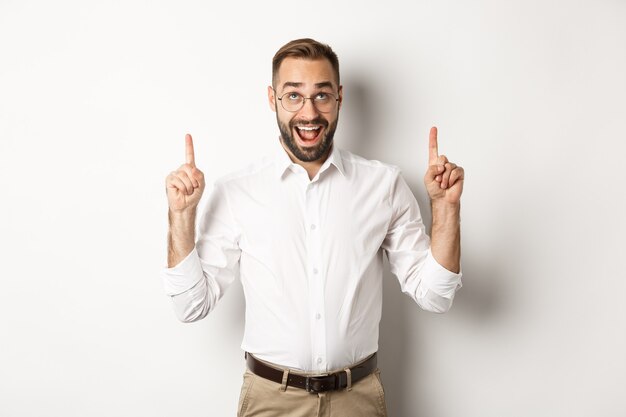 Hombre de negocios emocionado mirando publicidad, apuntando y mirando hacia arriba con cara feliz, de pie