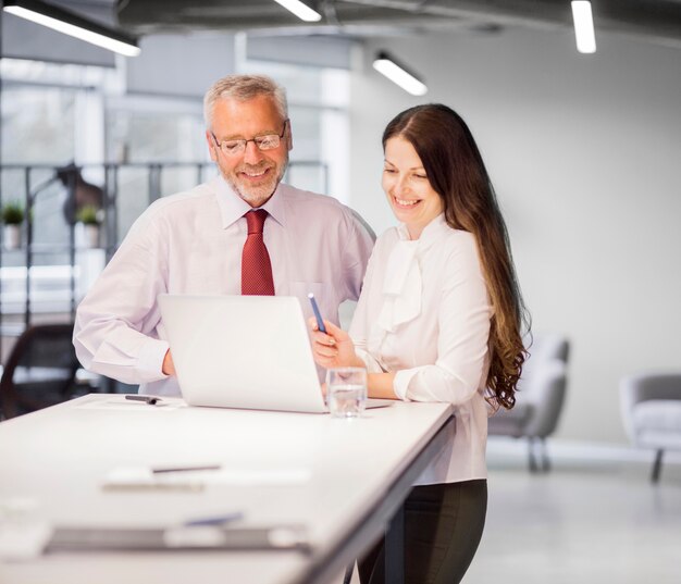 Hombre de negocios y empresaria sonrientes confiados que miran el ordenador portátil en la oficina