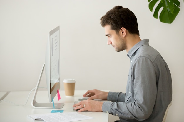 Foto gratuita hombre de negocios enfocado que trabaja en la computadora con estadísticas del proyecto, vista lateral