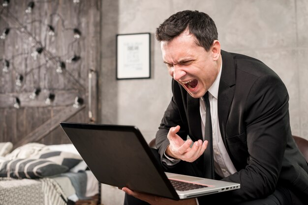 Hombre de negocios enojado que grita en el ordenador portátil en casa