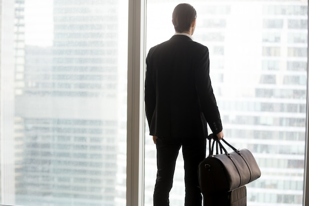 Hombre de negocios con el equipaje que se coloca delante de ventana grande.