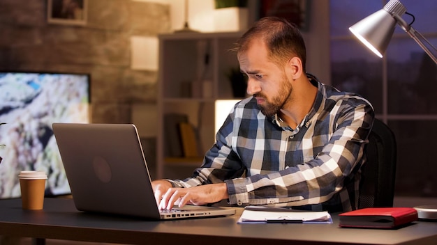 Hombre de negocios escribiendo en la computadora portátil y buscando documentos mientras trabaja desde la oficina en casa.