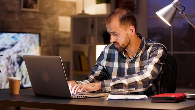 Hombre de negocios escribiendo en la computadora portátil y buscando documentos mientras trabaja desde la oficina en casa.