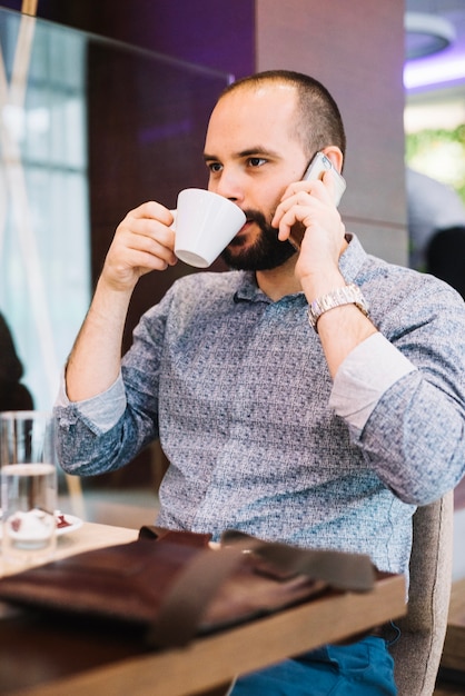 Hombre de negocios con estilo teniendo café durante la conversación telefónica