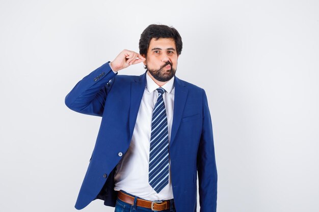 Foto gratuita hombre de negocios estirando la oreja y resoplando las mejillas en traje formal y con aspecto divertido. vista frontal.