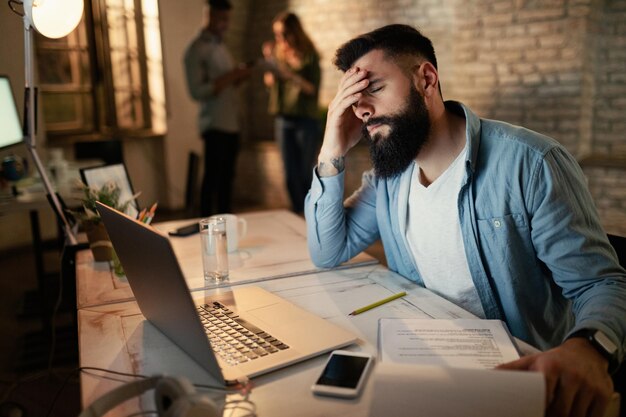 Hombre de negocios exhausto sosteniendo su cabeza con dolor mientras trabajaba hasta tarde en la oficina
