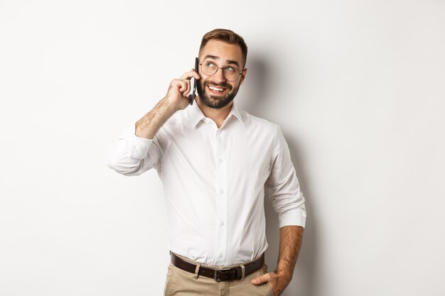 Hombre de negocios exitoso en gafas hablando por teléfono móvil, mirando satisfecho y sonriendo, de pie