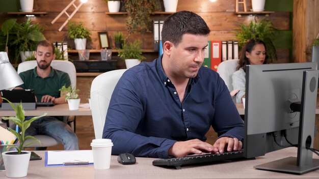 Hombre de negocios exitoso sentado en el escritorio escribiendo estrategia de marketing en el teclado de la computadora trabajando en un proyecto empresarial en la oficina de la empresa de inicio. Mujer emprendedora analizando presentación de gestión