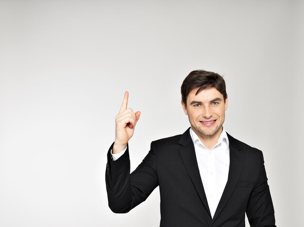 Hombre de negocios feliz apunta su dedo hacia arriba en traje negro