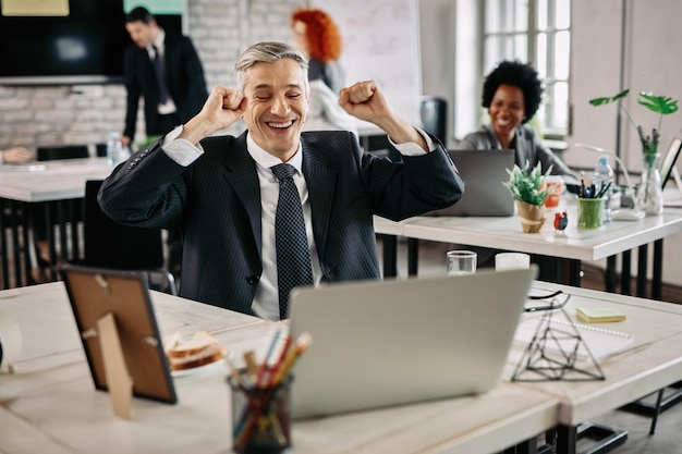 Hombre de negocios feliz celebrando el éxito mientras trabaja en la computadora en la oficina