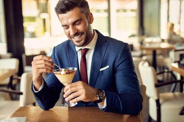 Hombre de negocios feliz comiendo postre mientras se relaja en un café