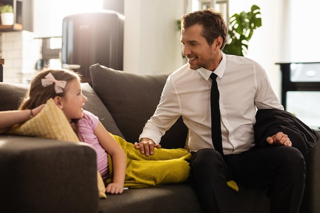 Un hombre de negocios feliz comunicándose con una hija mientras se sienta en el sofá de la sala de estar